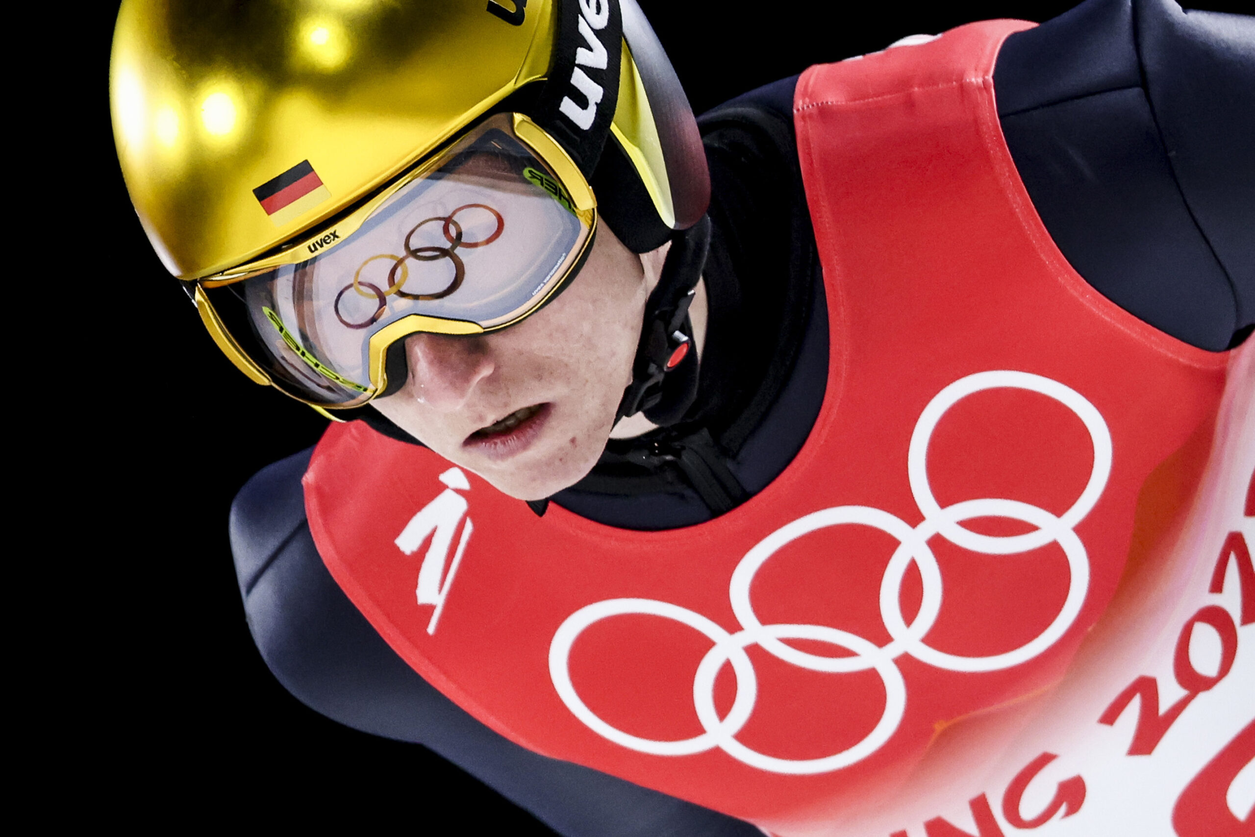 在北京2022年冬奥会男子资格项目北欧跳台滑雪大丘上，卡尔·盖革护目镜上的奥运五环映照出来。