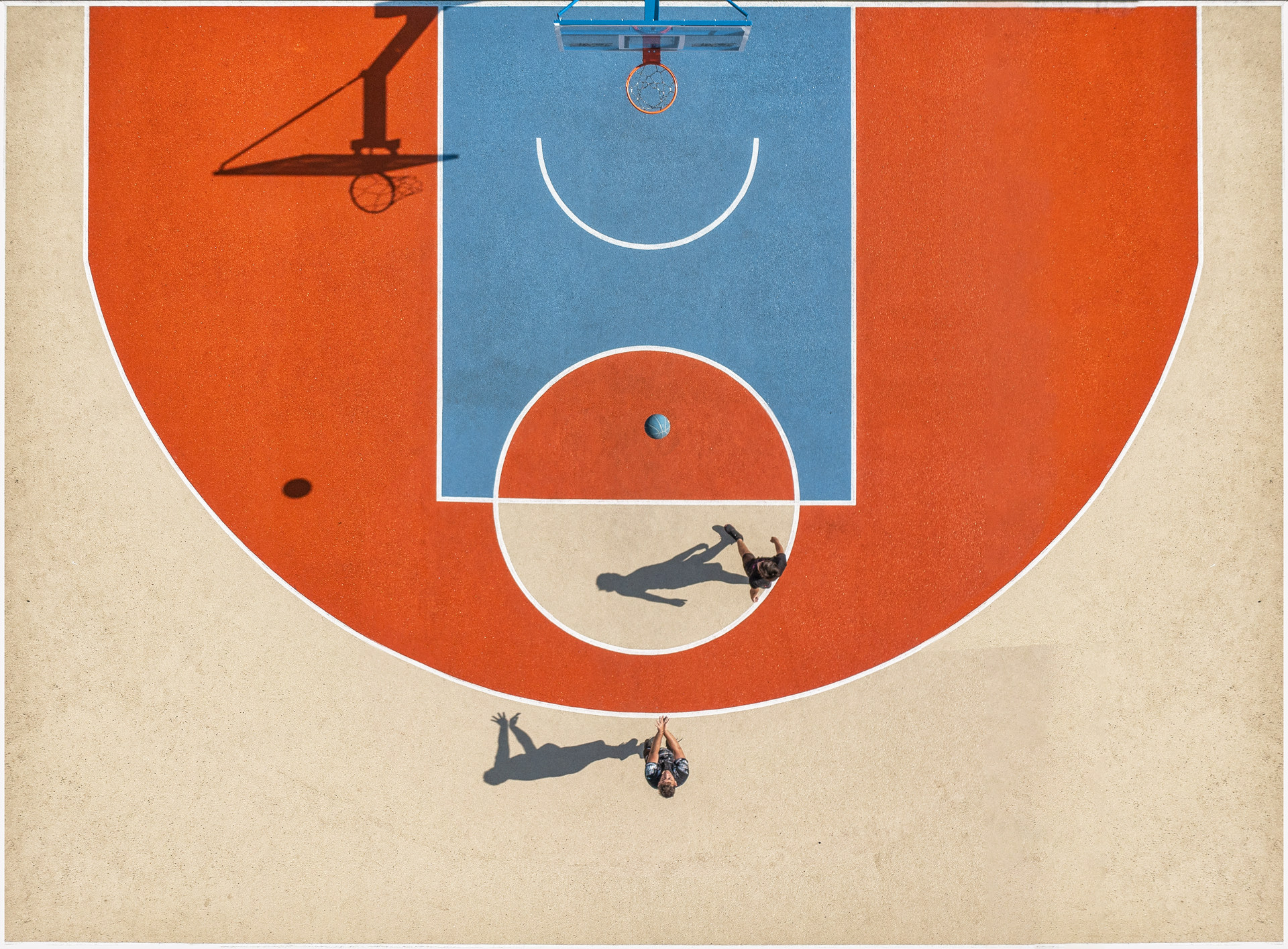 两个人站在橙、蓝、棕三色的篮球场上，从上面看。