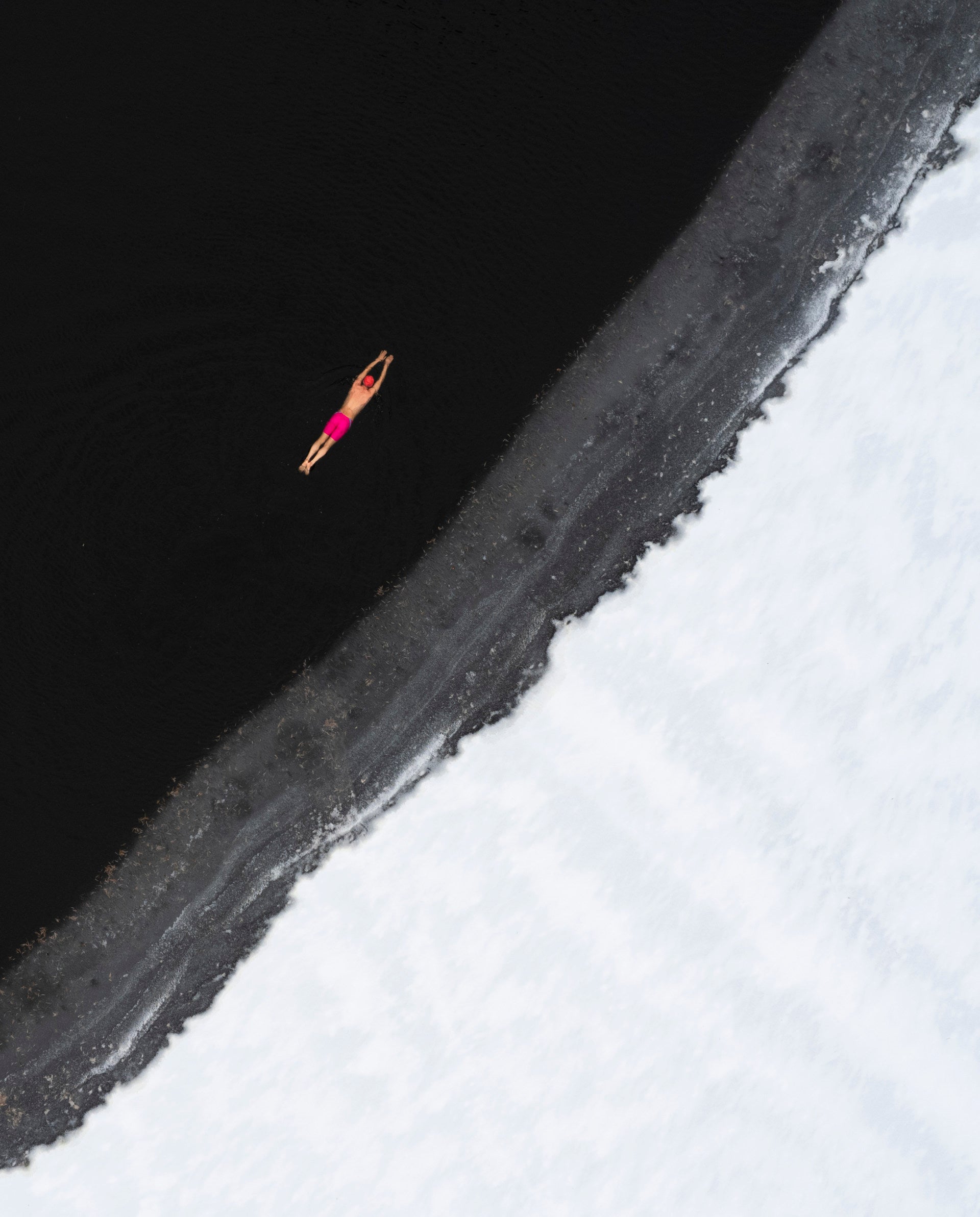 一名身穿粉色泳衣的男子在几乎结冰的水中游泳。
